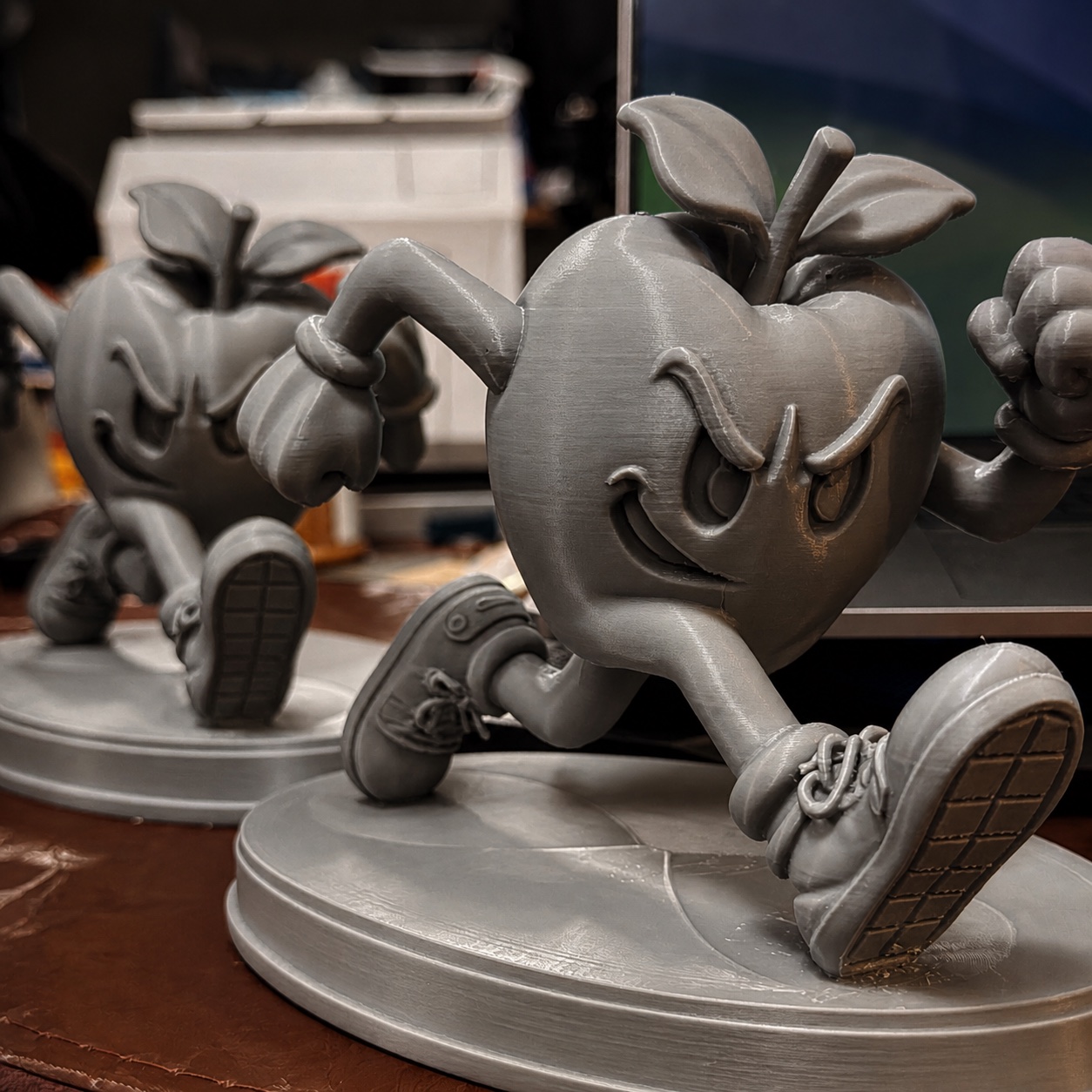 Two custom gray 3D-printed running apple character sculptures